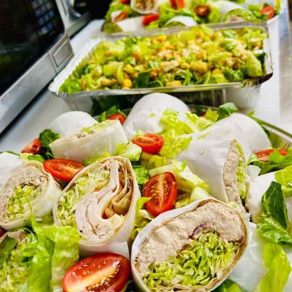 Assortment of wraps and salads in catering trays, ready for serving.