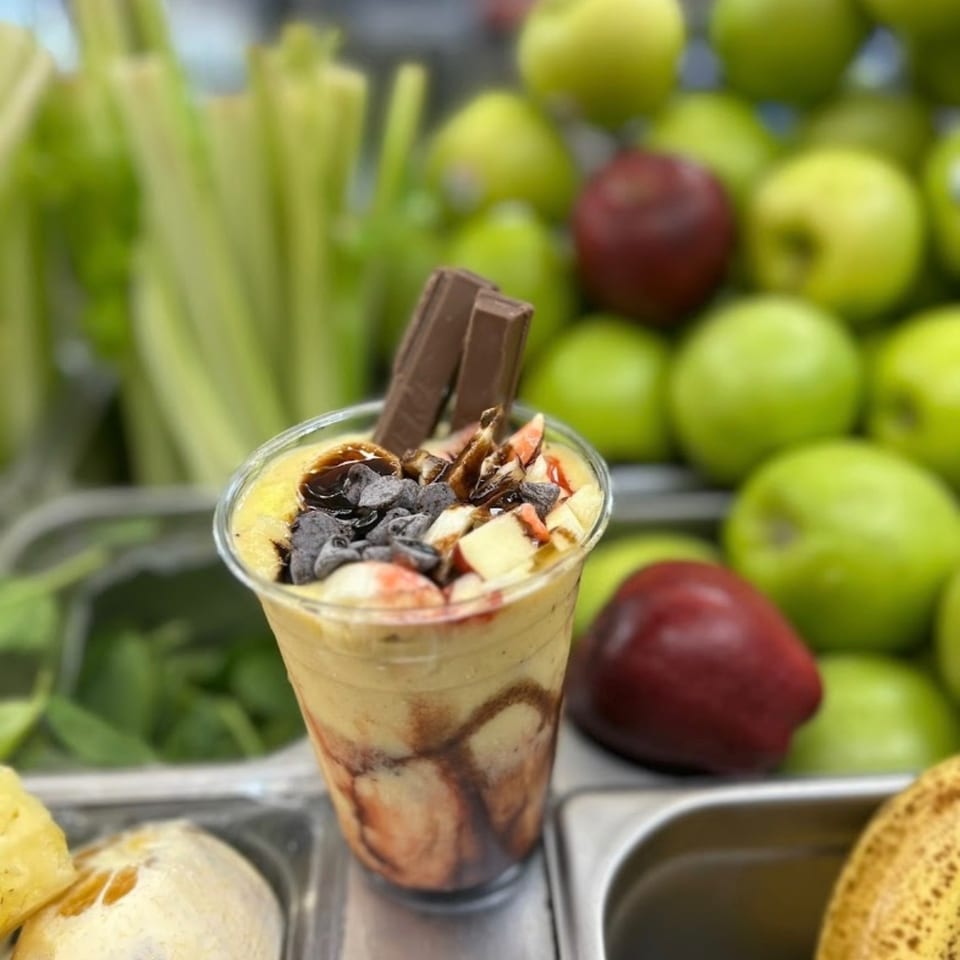 A smoothie with chocolate, fruit, and Kit Kat bars, surrounded by fresh produce like apples and celery.