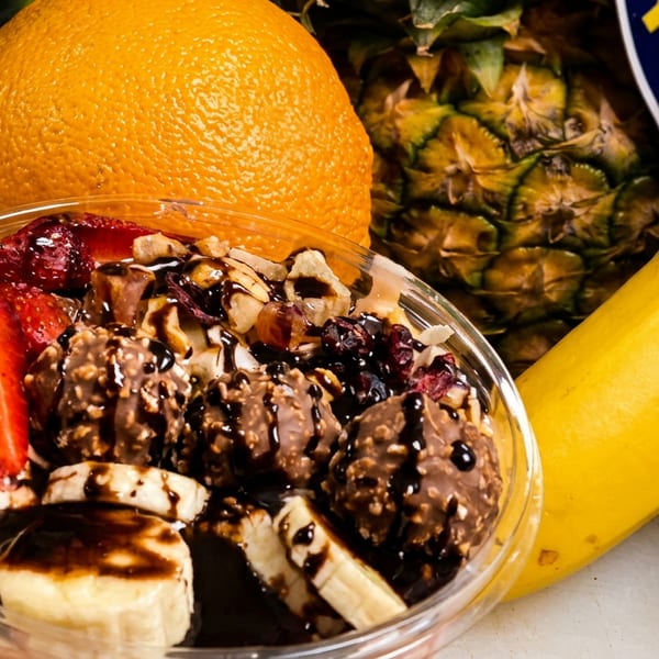 Fruit bowl with strawberries, bananas, chocolate, and nuts, surrounded by fresh fruit.