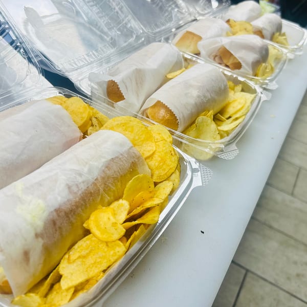 Several clear plastic containers with wrapped sandwiches and potato chips on a white counter.