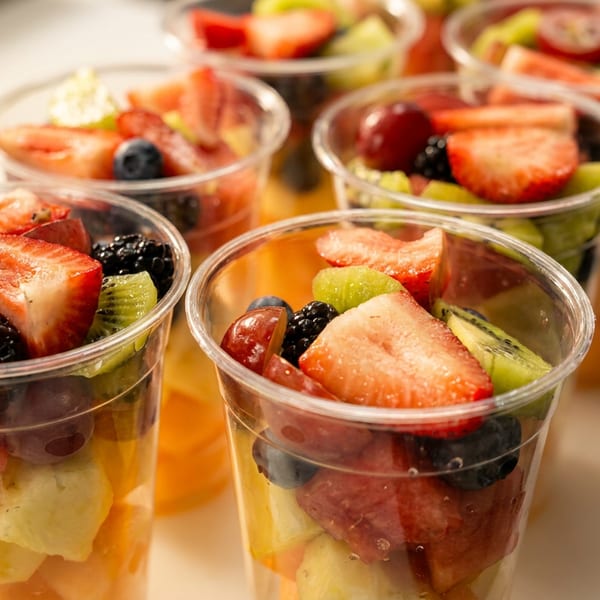 Rows of clear plastic cups filled with fresh fruit salad, including strawberries, kiwi, and berries.