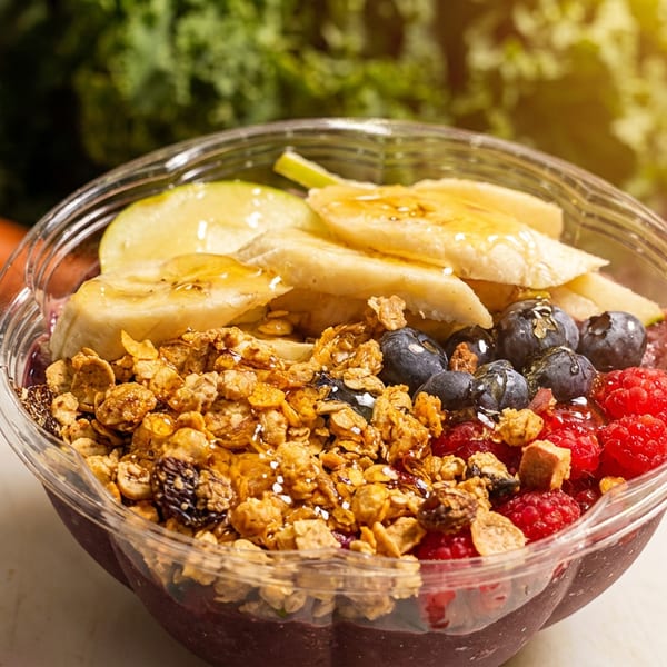 A vibrant acai bowl topped with granola, banana slices, blueberries, and raspberries, drizzled with honey.