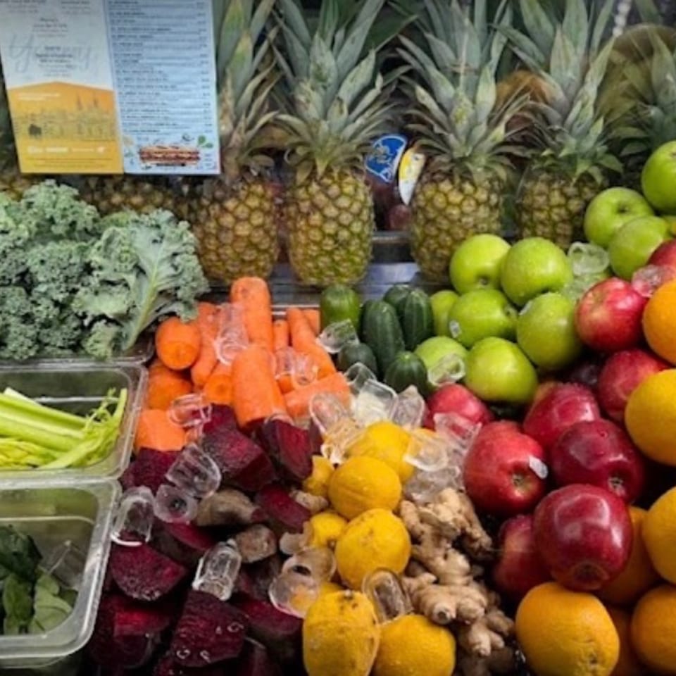 Fresh fruits and vegetables, including pineapples, kale, celery, spinach, carrots, and apples, on display.