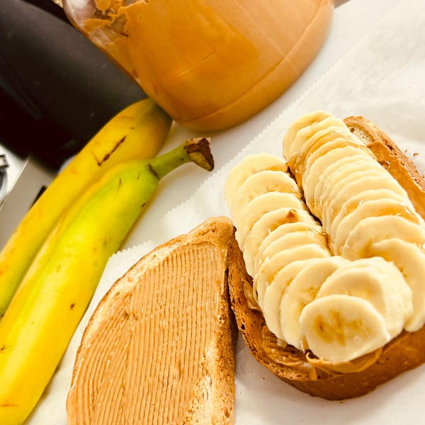 Peanut butter jar, two bananas, and two slices of toast with peanut butter and banana slices.