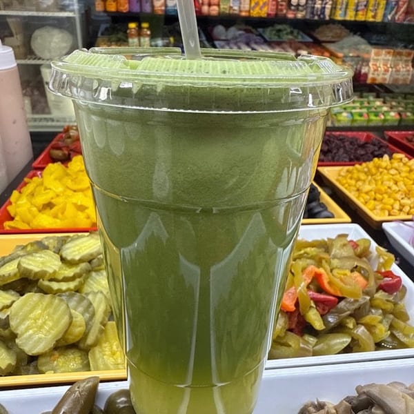 Green smoothie in a clear cup with a straw, surrounded by various deli toppings.