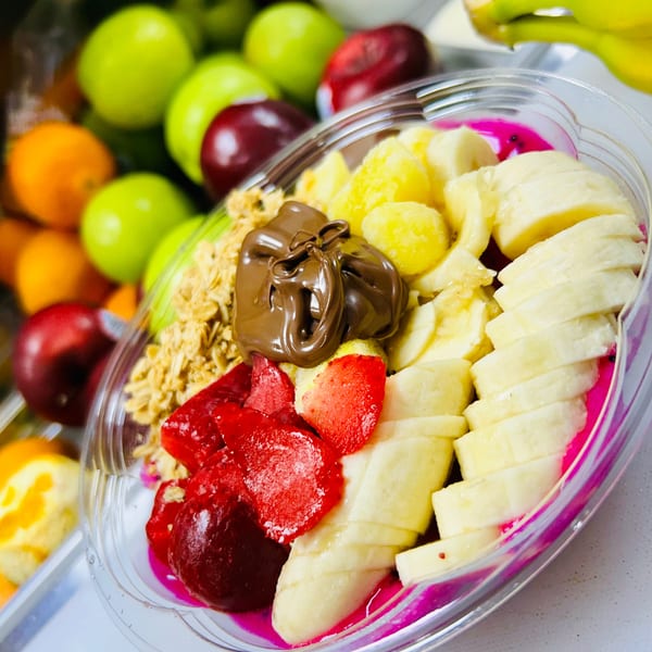 A vibrant fruit bowl with bananas, strawberries, granola, pineapple, and chocolate drizzle.