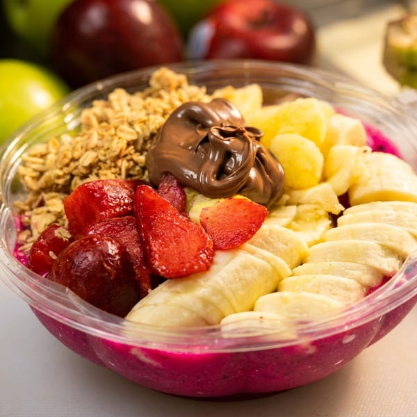 A vibrant dragon fruit smoothie bowl topped with granola, strawberries, bananas, pineapple, and Nutella.