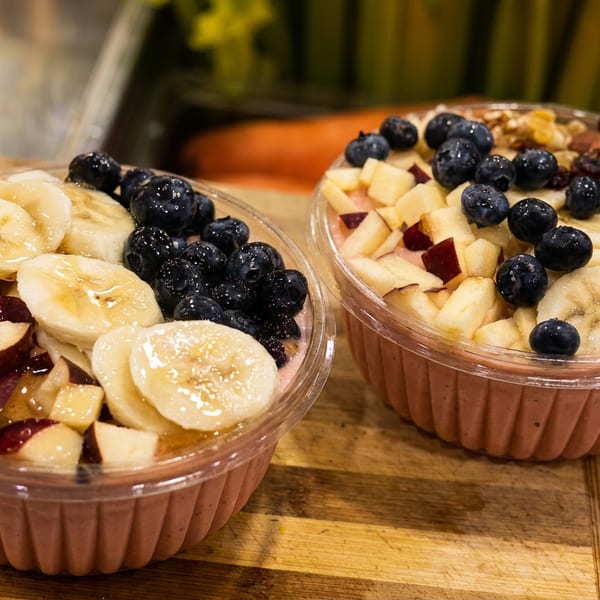 Two vibrant smoothie bowls topped with fresh fruit, nuts, and berries on a wooden board.