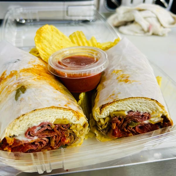 Two halves of a deli sandwich with chips and a dipping sauce in a plastic container.