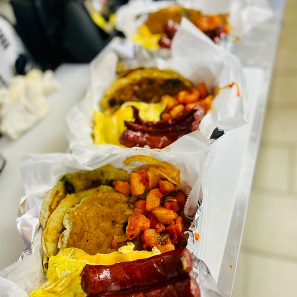Multiple breakfast platters with pancakes, scrambled eggs, sausage, and home fries in foil containers.