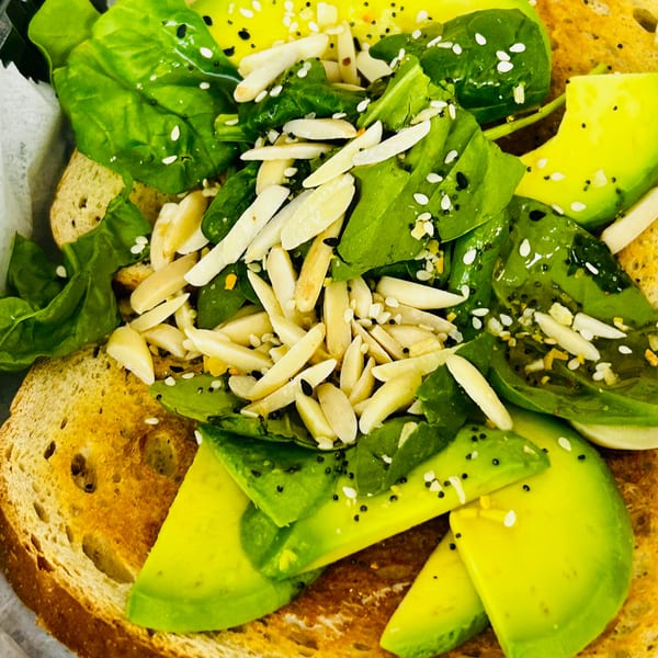 Avocado toast topped with spinach, sliced almonds, poppy seeds, and sesame seeds.
