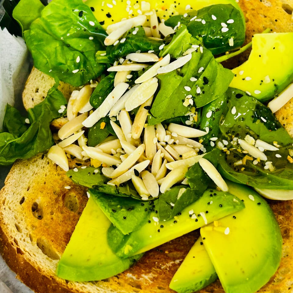 Avocado toast topped with spinach, sliced almonds, poppy seeds, and sesame seeds.