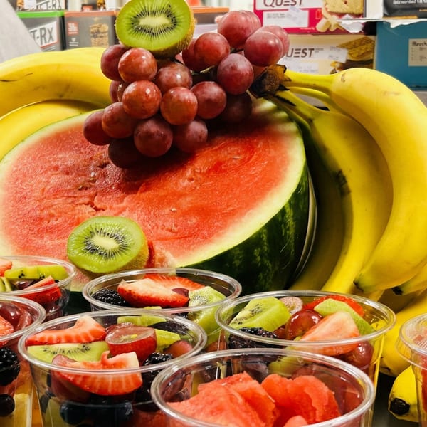 Fresh fruit display with bananas, watermelon, grapes, kiwi, and fruit cups filled with berries.