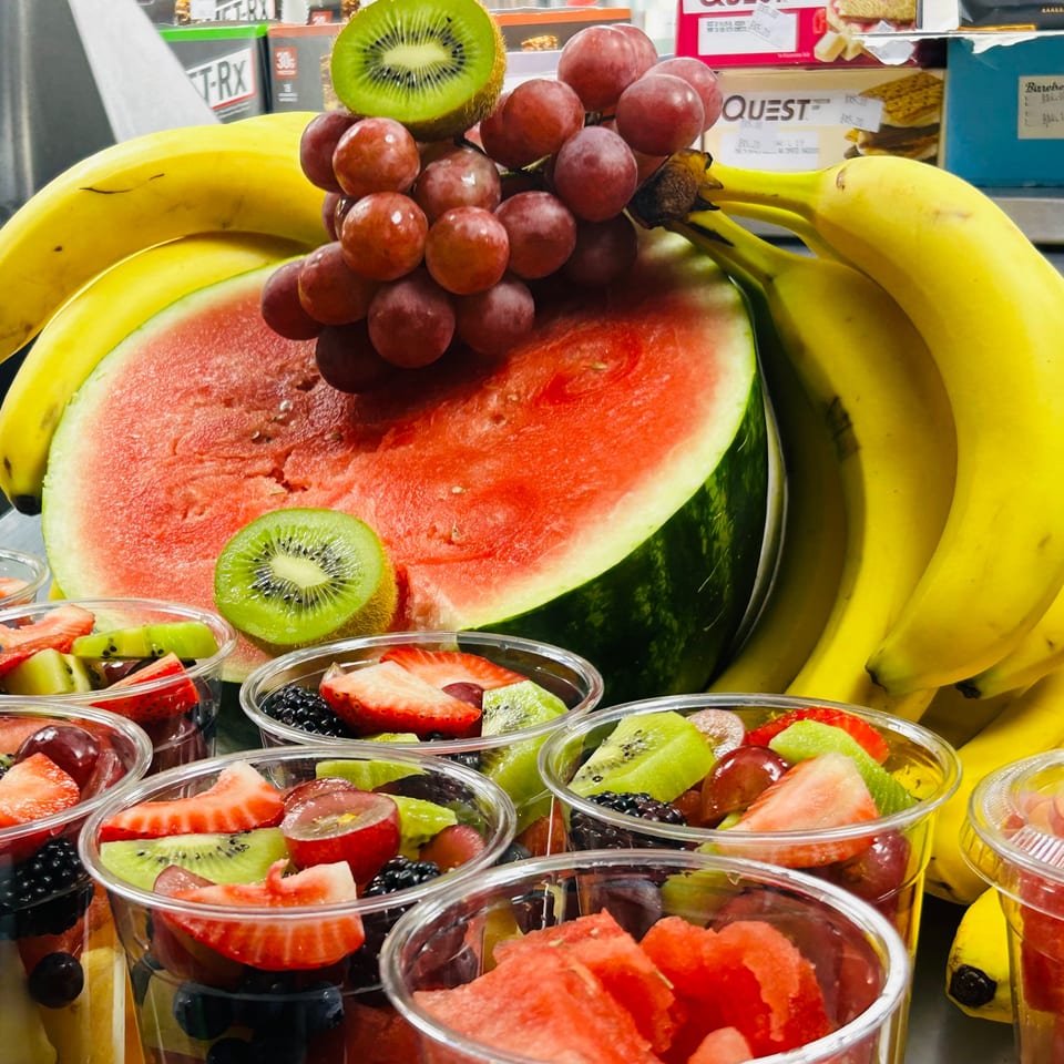 Fresh fruit display with bananas, watermelon, grapes, kiwi, and fruit cups.